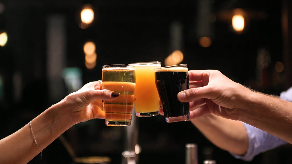Manos brindando con vasos de cata de cervezas de distintos colores